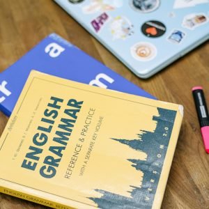 High-angle view of an English grammar book and a laptop with stickers on a wooden desk.
