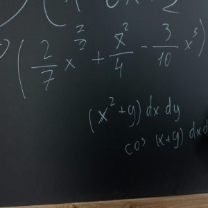 Hand writing mathematical equations on a chalkboard in a classroom setting.